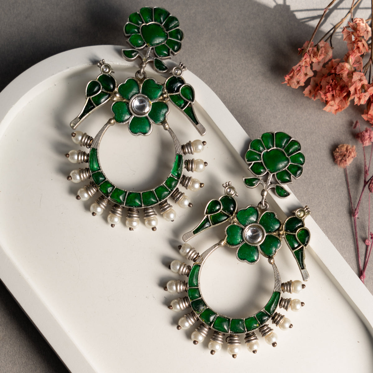 A pair of faux silver earrings with green accents and a floral design, displayed on a white surface.
